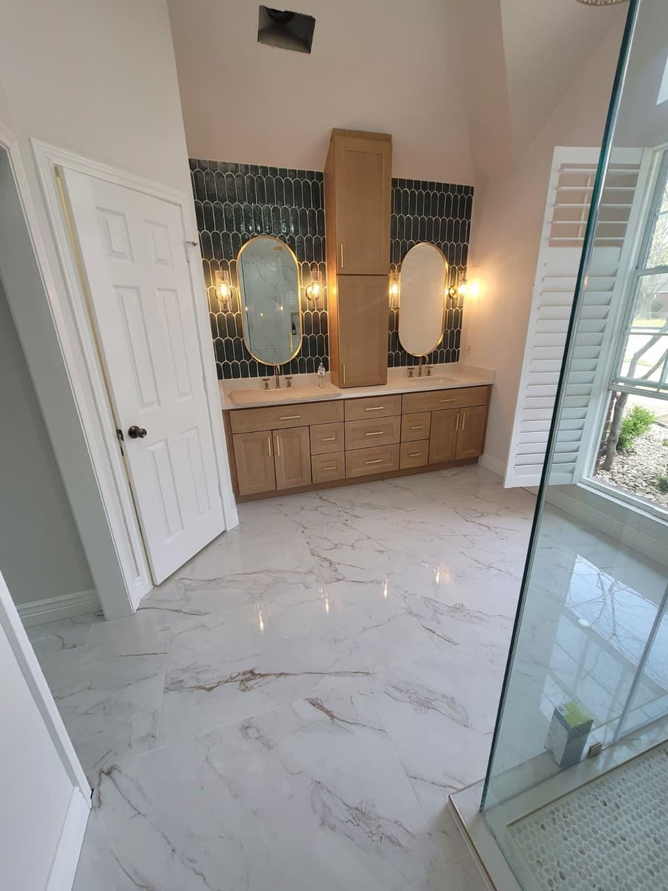 Primary bathroom remodel with a frameless glass shower, marble-look tile, green picket tile vanity wall and a chandelier
