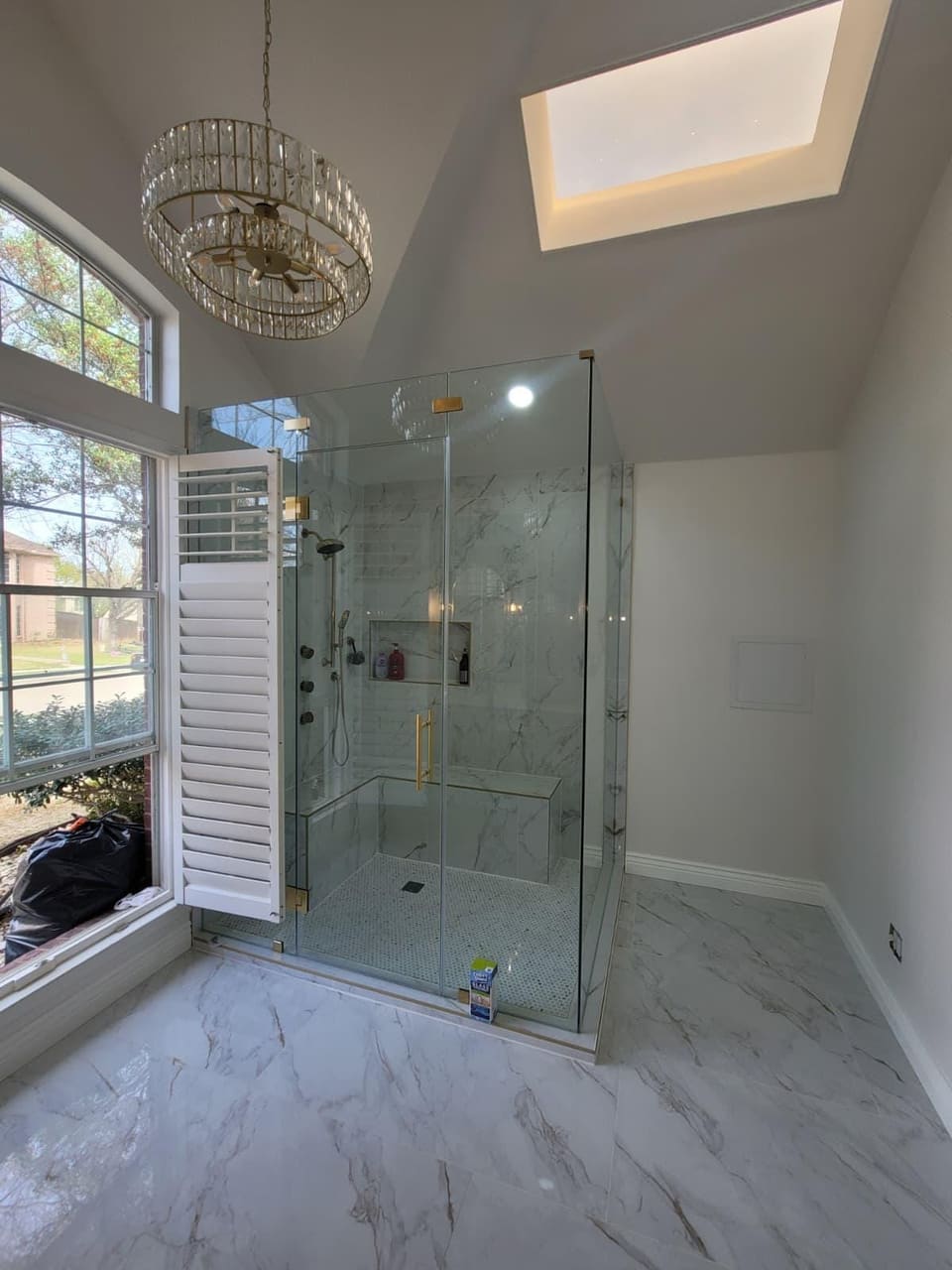 Frameless glass walk-in shower with a tiled bench, niche and mosaic floor in a remodeled primary bathroom