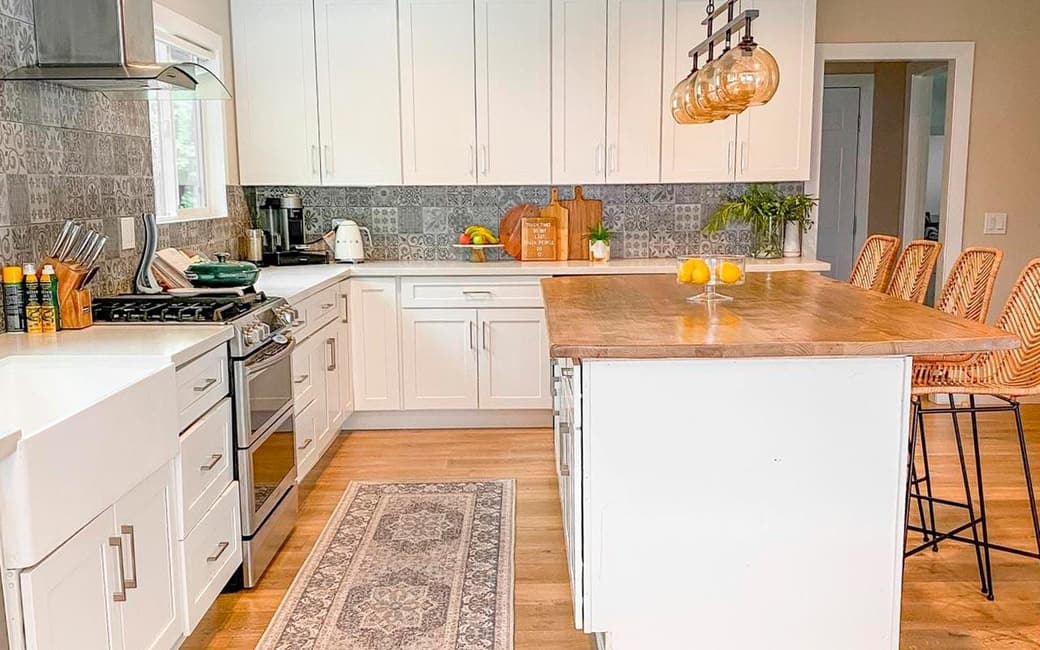 Kitchen with white shaker cabinets, patterned tile backsplash, farmhouse sink and a butcher-block island with rattan stools